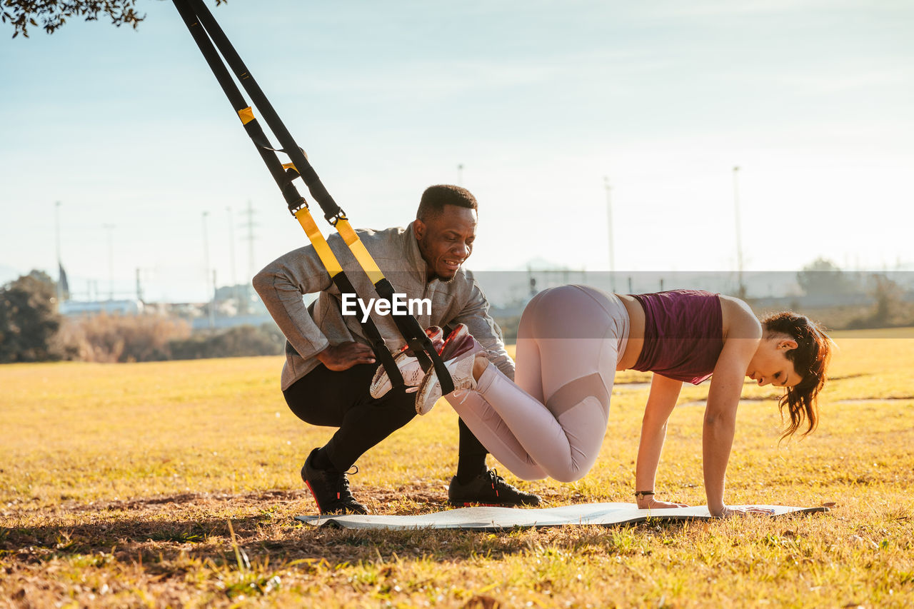 Full length of man assisting friend in exercising at public park