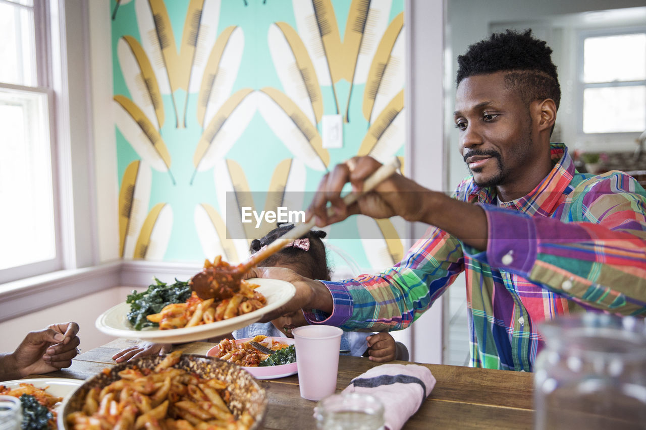 Man serving food in plate while having meal with family at home