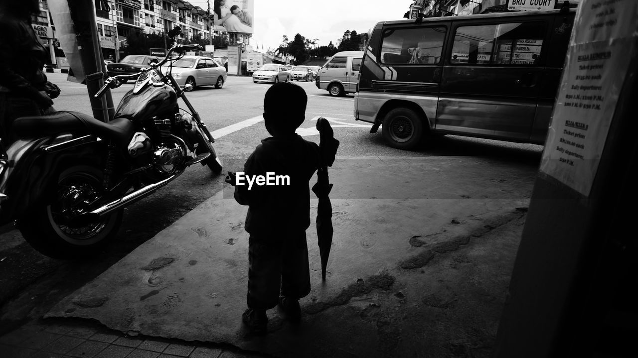 Rear view of boy standing with umbrella on street