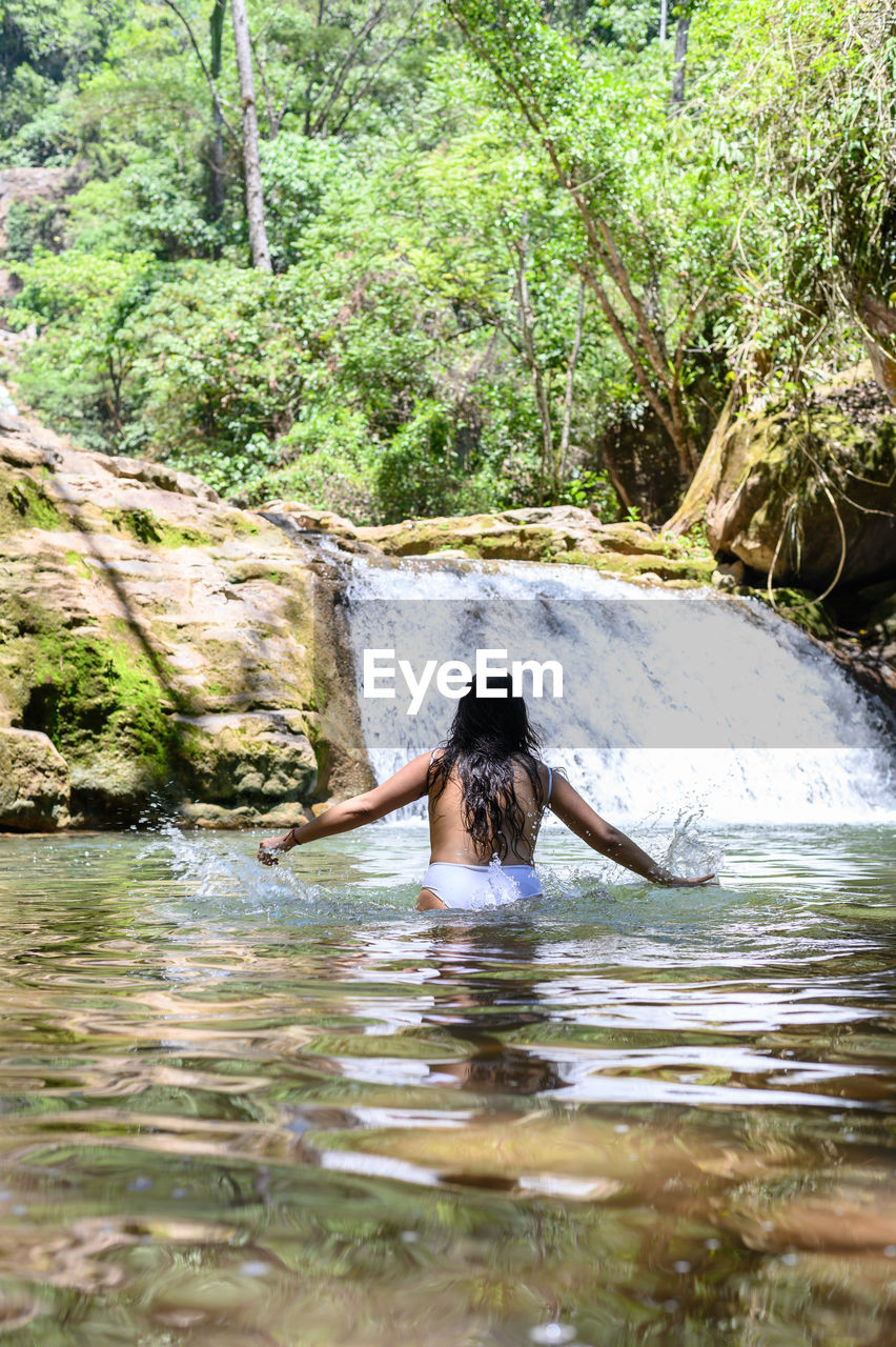 water, river, one person, tree, nature, plant, jungle, leisure activity, forest, beauty in nature, day, adult, women, lifestyles, young adult, holiday, vacation, trip, stream, outdoors, tranquility, wilderness, rainforest, waterfront, land, rear view, green, tranquil scene, scenics - nature, non-urban scene, relaxation, enjoyment, motion, rock, long hair, person, boating, travel, growth, environment, sunlight, adventure, portrait