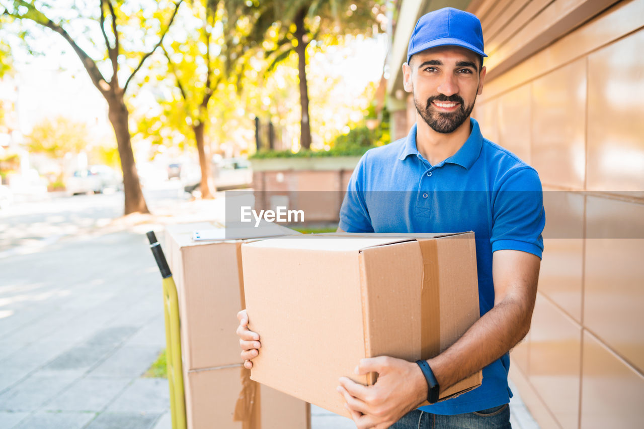 PORTRAIT OF SMILING YOUNG MAN STANDING ON BOX