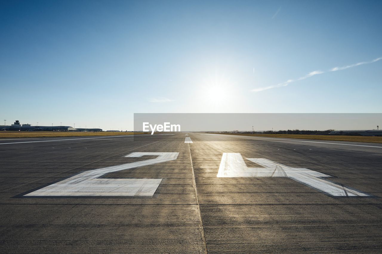 Surface level of airport runway with road marking and number 24 against clear sky.