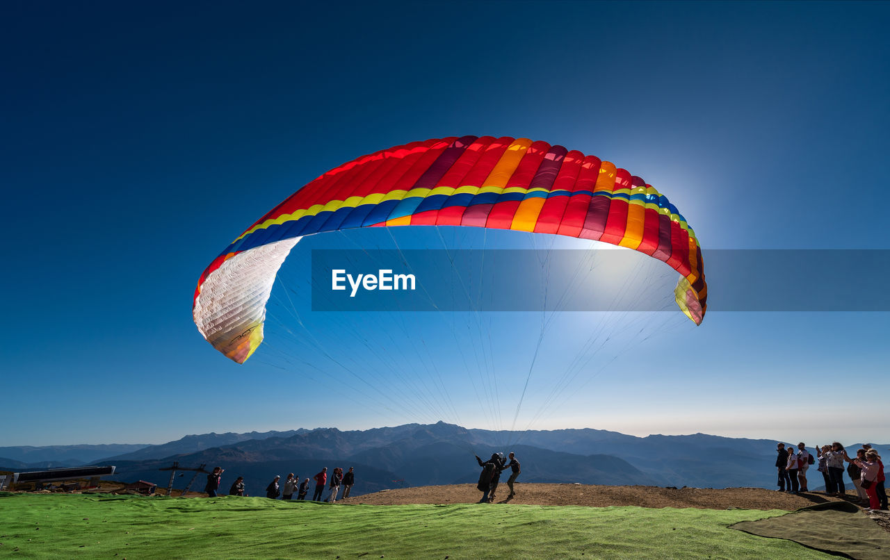 PEOPLE FLYING KITE AGAINST CLEAR SKY