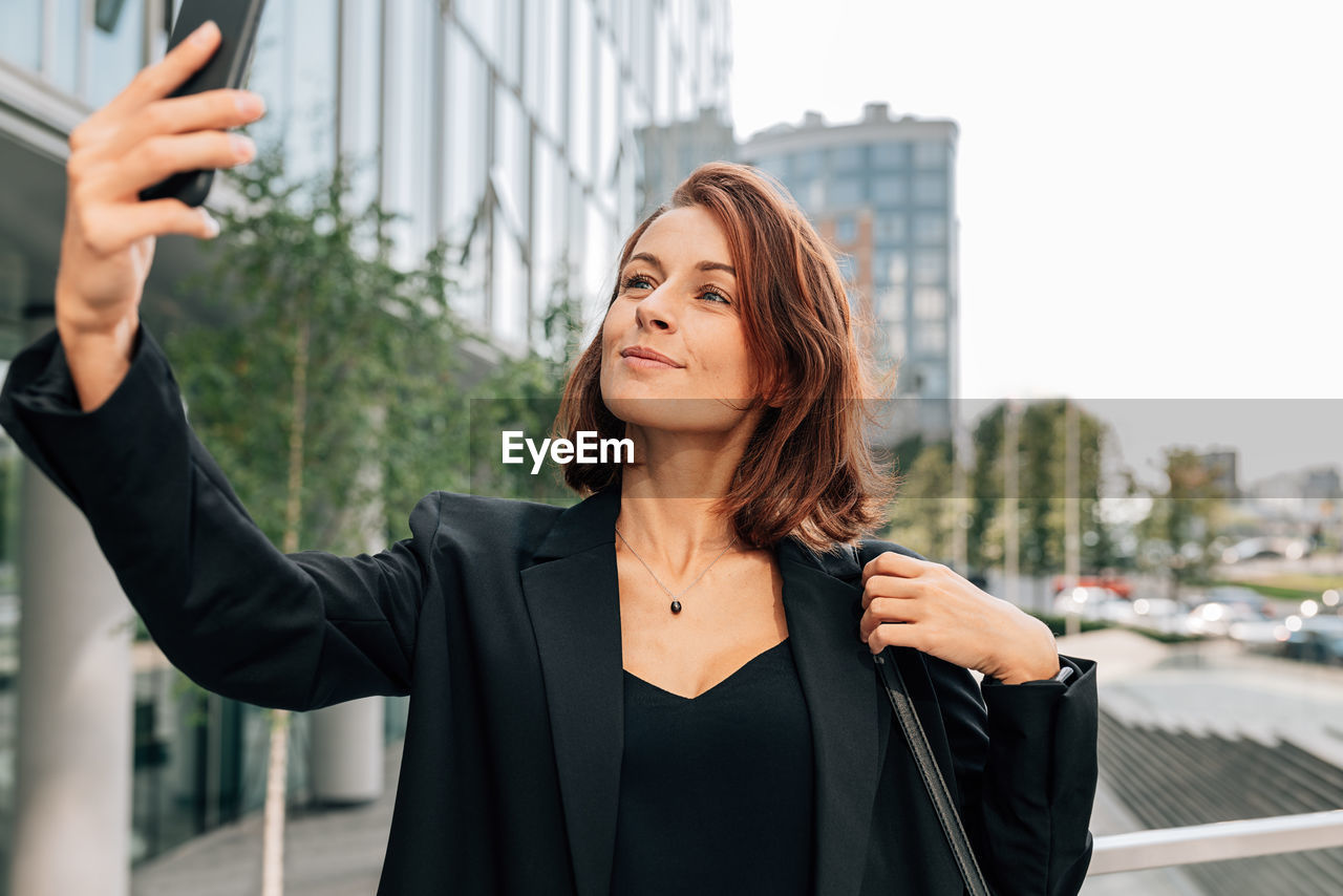 portrait of young woman looking away against buildings in city