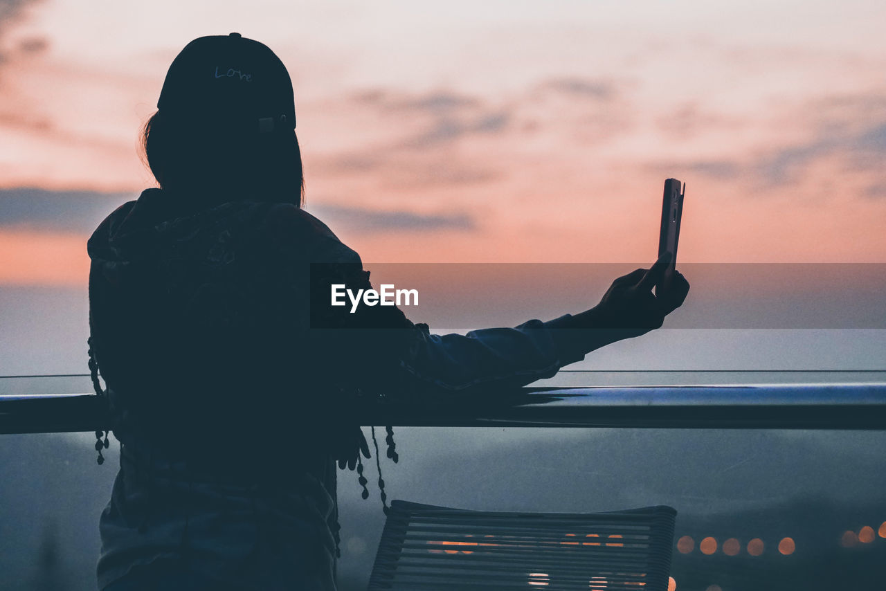 Woman taking selfie against sky during sunset