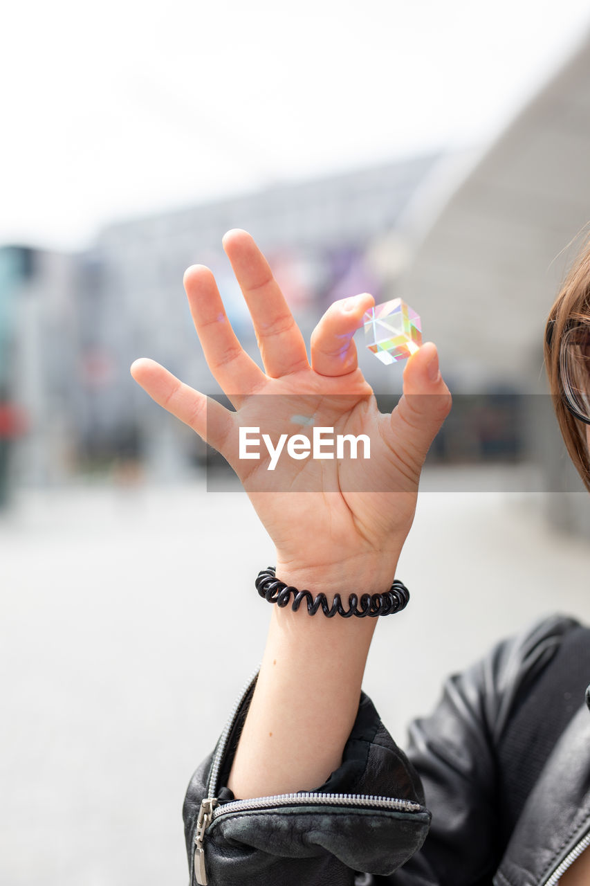 MIDSECTION OF WOMAN HOLDING HANDS AGAINST BLURRED BACKGROUND