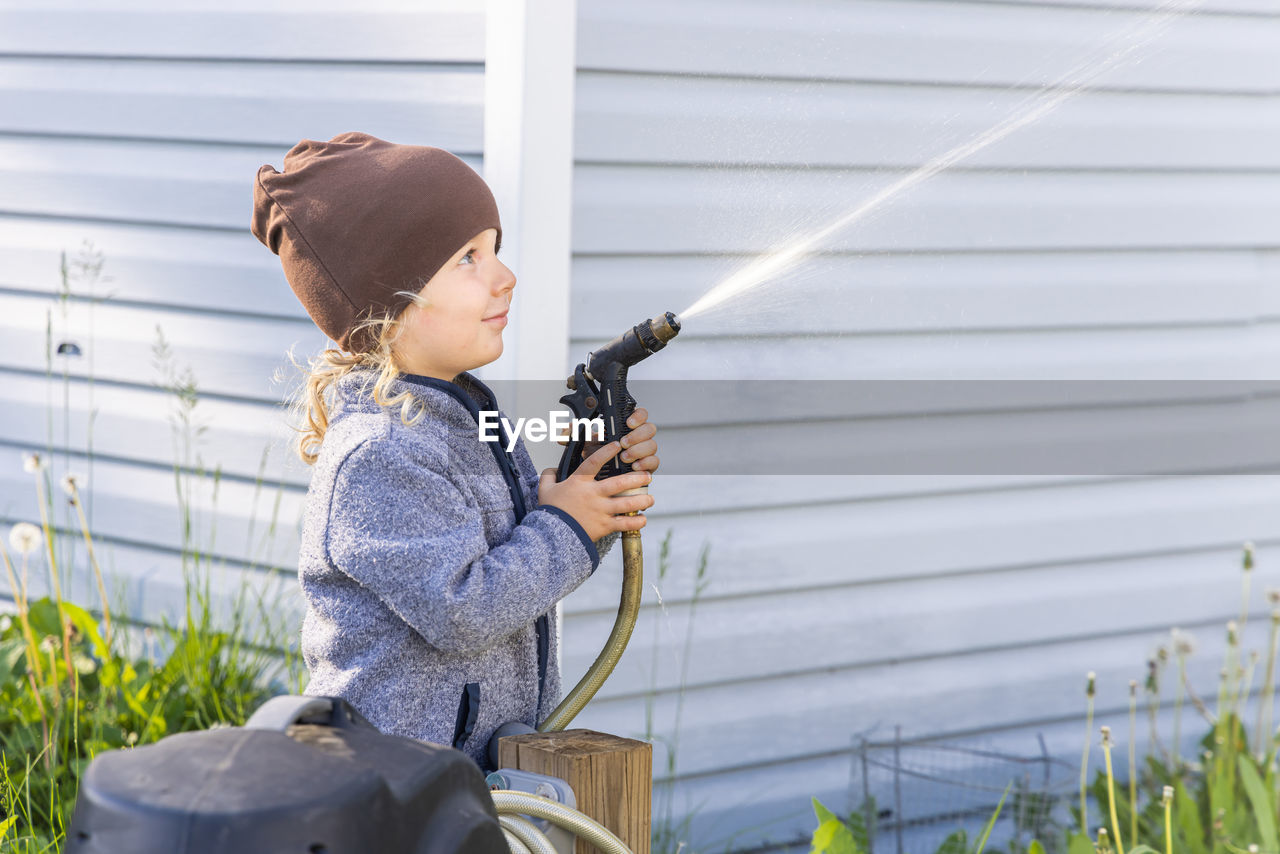 Side view of boy holding water hose