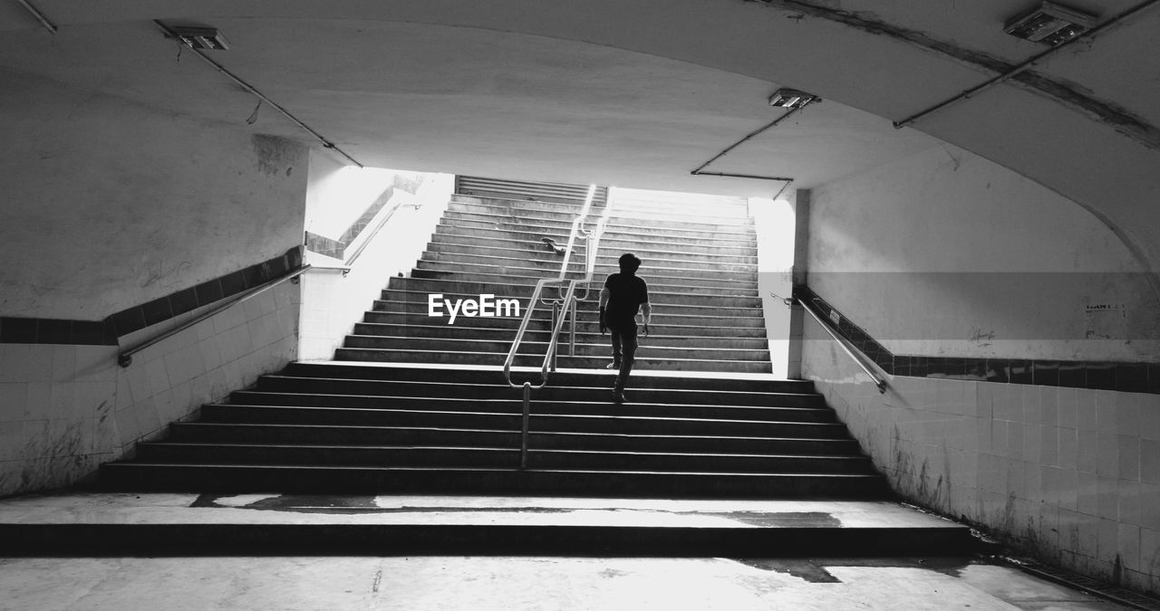 REAR VIEW OF MAN WALKING UP STAIRS