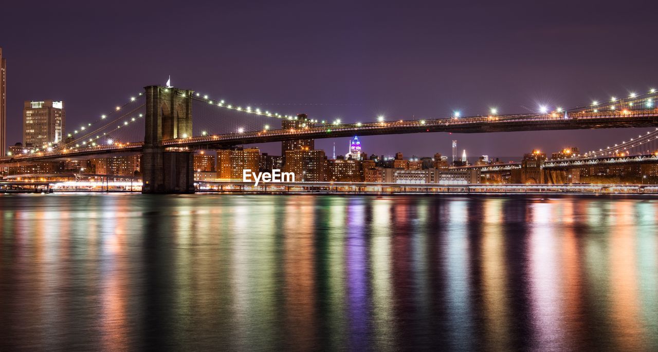 Brooklyn bridge over east river against sky in illuminated city at night
