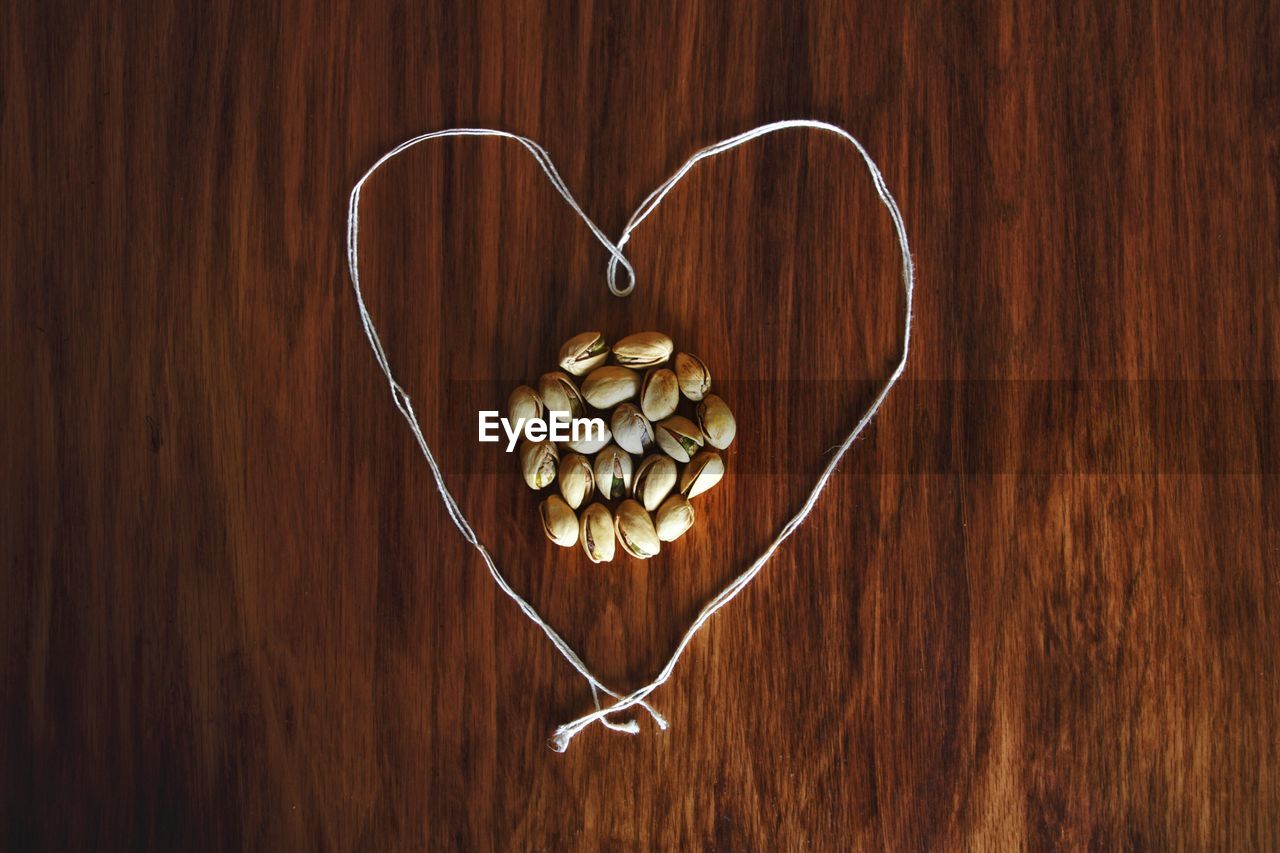 High angle view of pistachio by heart shape thread on wooden table
