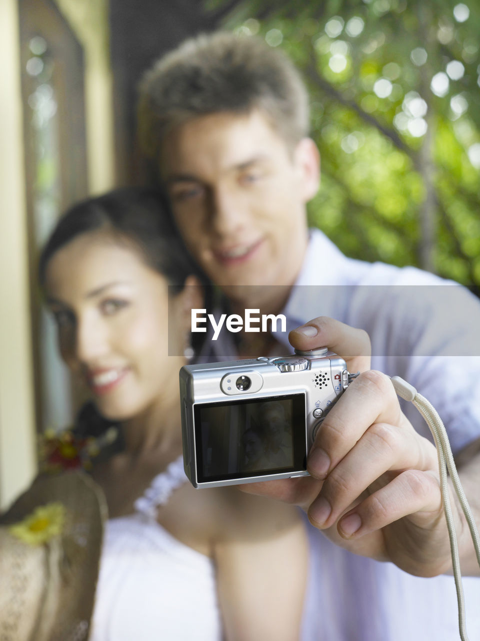 PORTRAIT OF SMILING YOUNG WOMAN USING MOBILE PHONE IN CAMERA