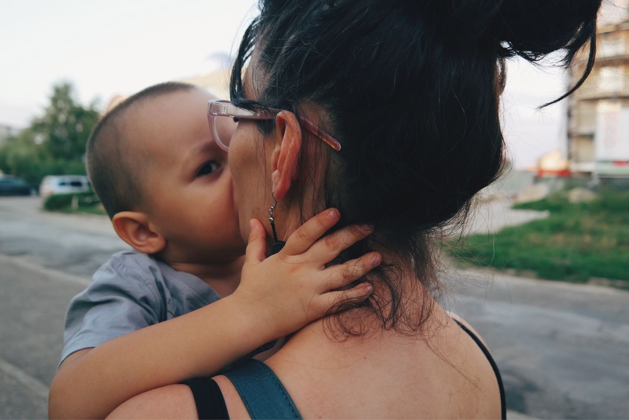 Baby boy kissing mother on street