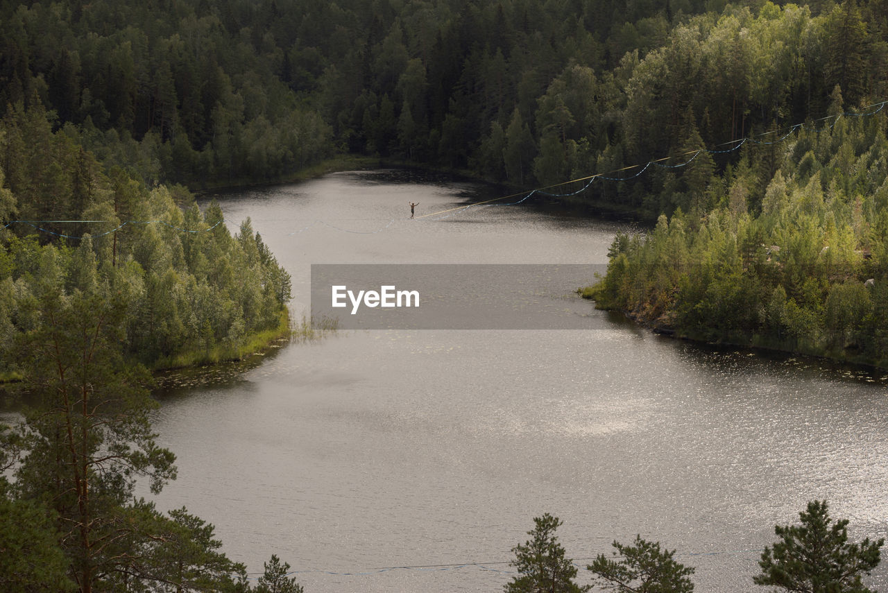 A tightrope walker on a slackline over a picturesque forest lake. extreme sports theme