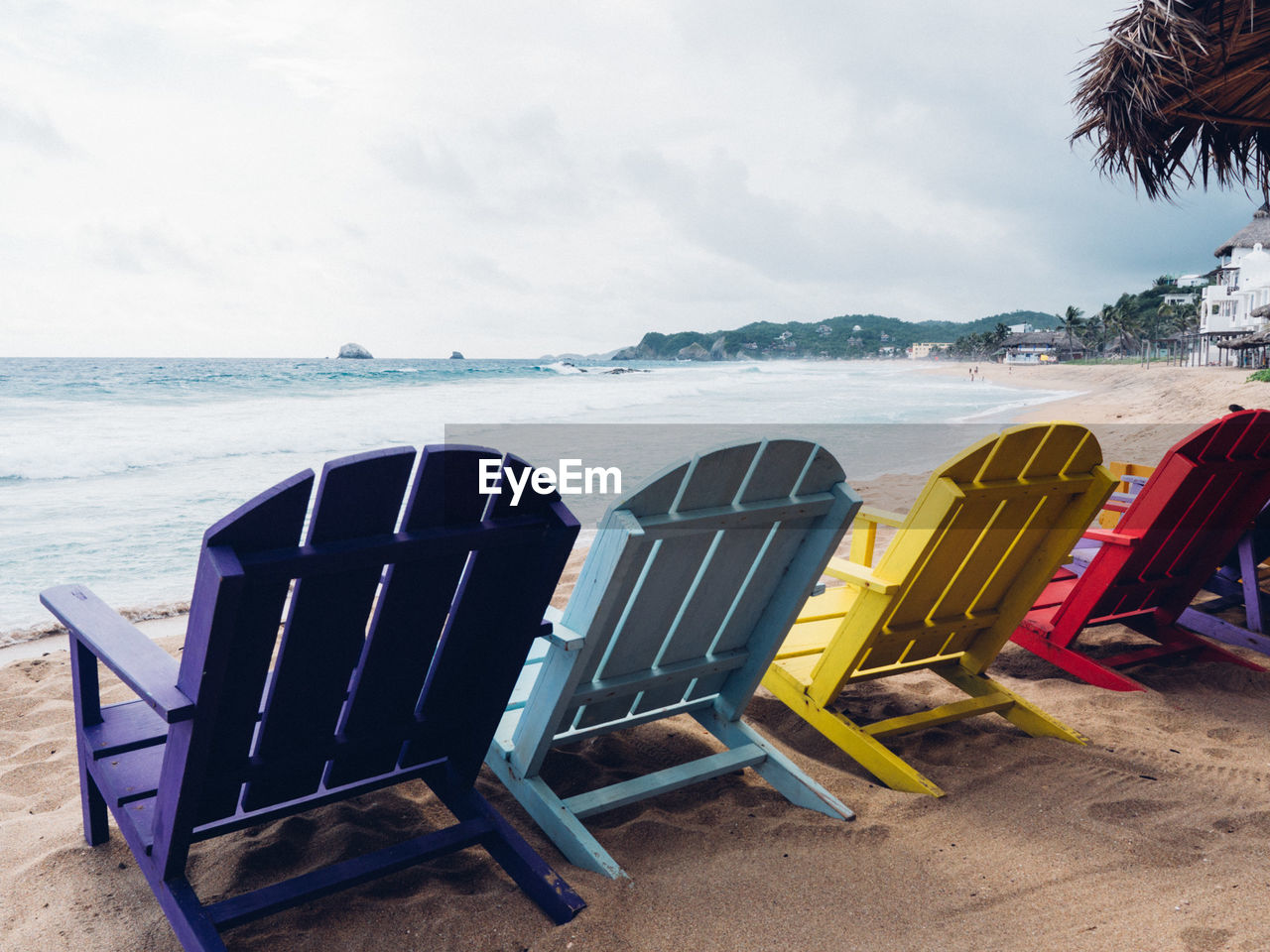 Colorful deck chairs on shore at beach against sky