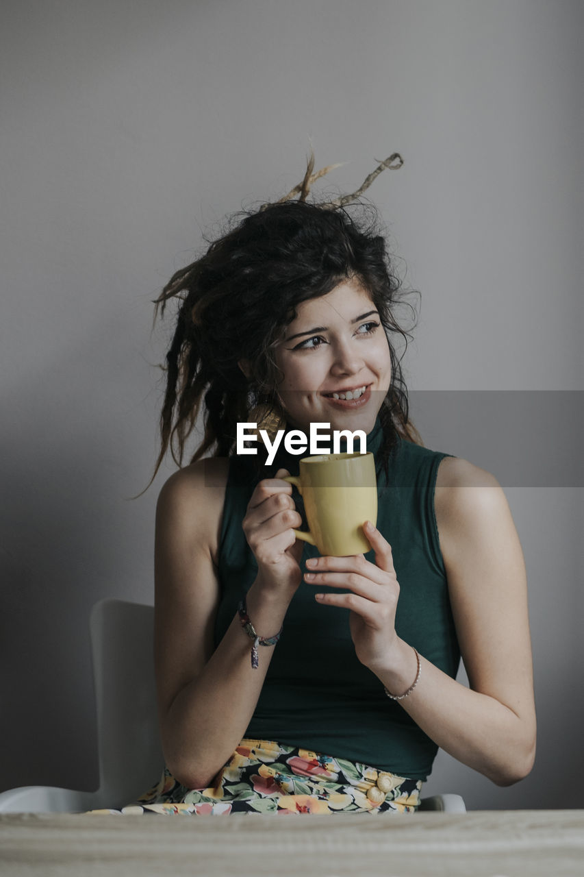 Close-up of young woman drinking coffee while sitting on chair against wall