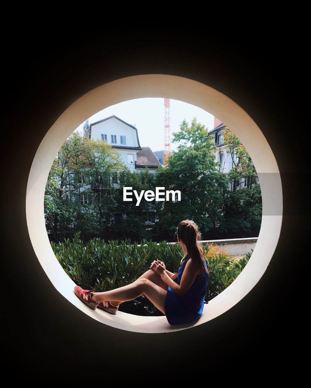 Side view of young woman sitting on circle shape window