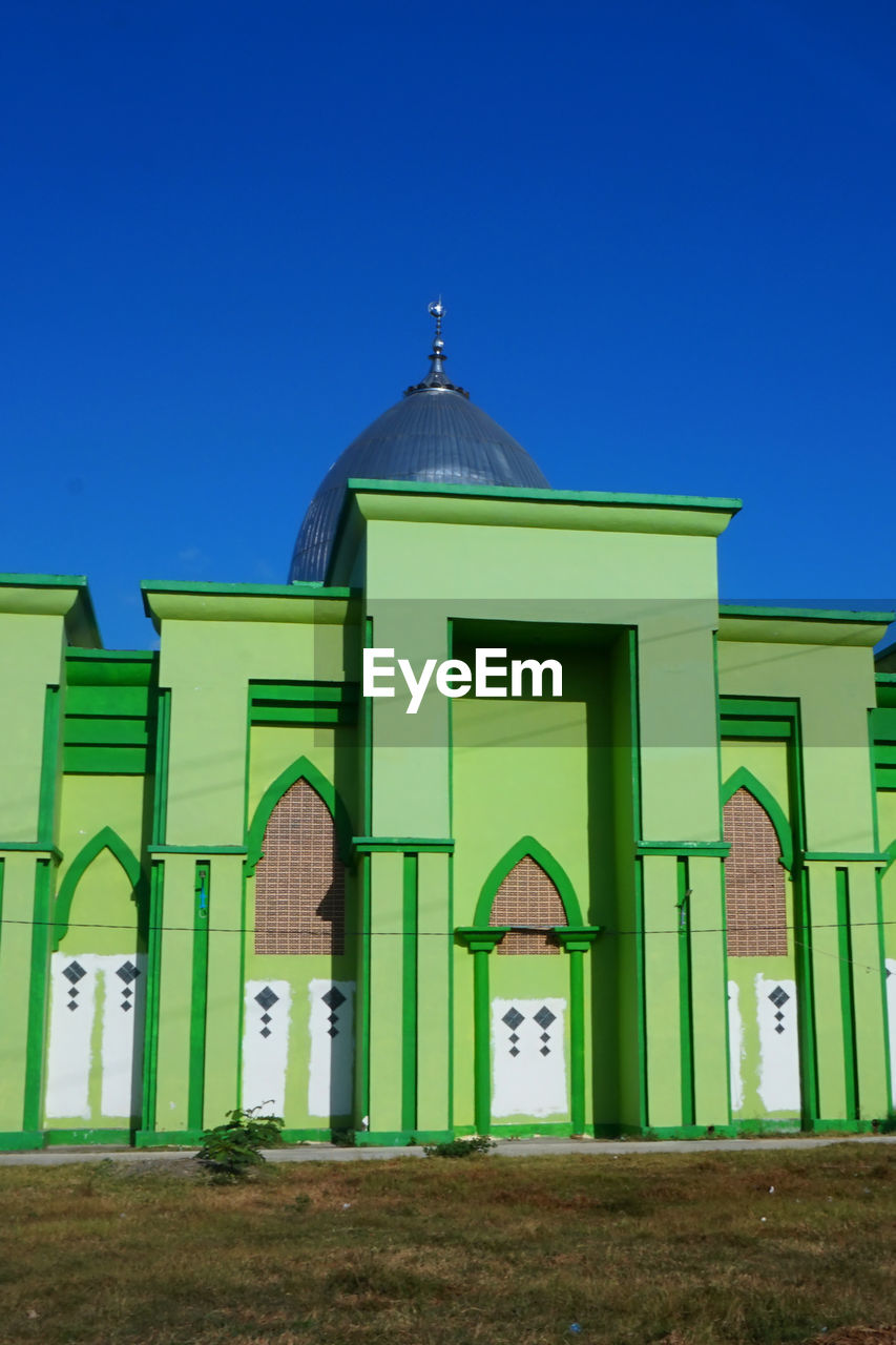 architecture, built structure, building exterior, building, place of worship, sky, religion, clear sky, blue, belief, no people, house, entrance, nature, green, spirituality, travel destinations, day, facade, door, grass, outdoors, arch, sunny, catholicism, history, the past, landmark