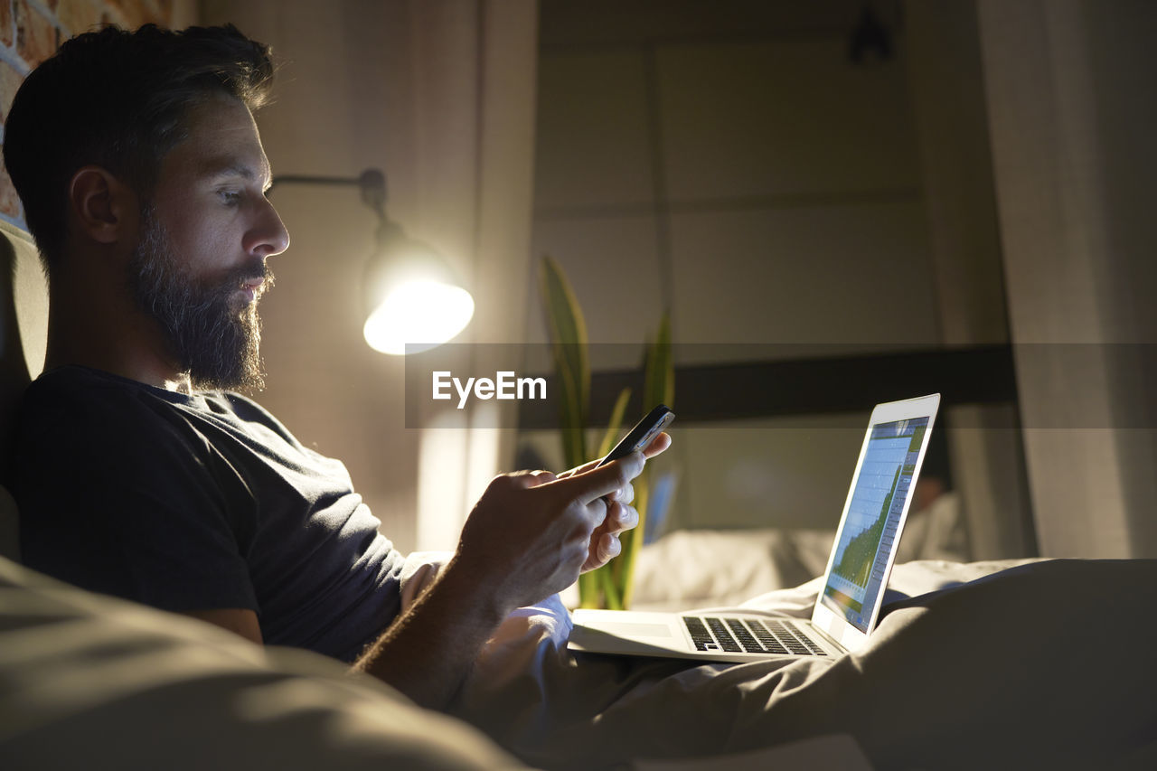 Side view of businessman using mobile phone while sitting by laptop