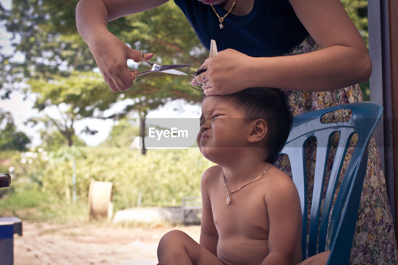 Midsection of woman cutting boy hair sitting on chair