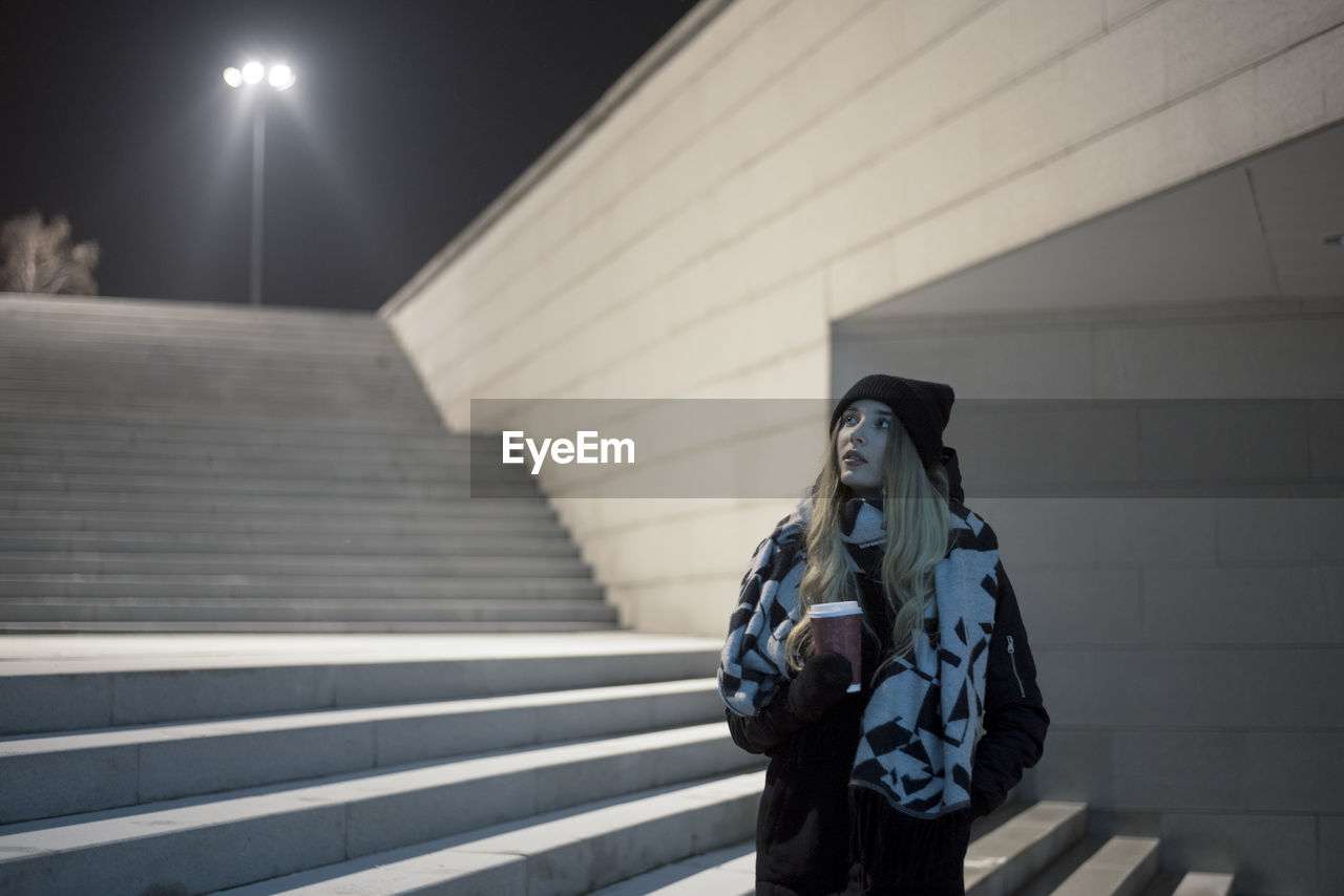 Woman looking away while standing in city at night