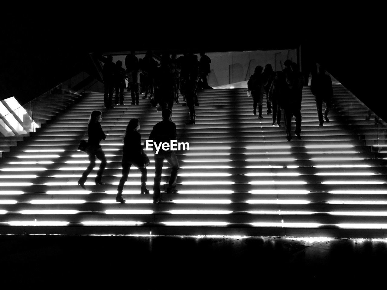 Silhouette people walking illuminated steps at night