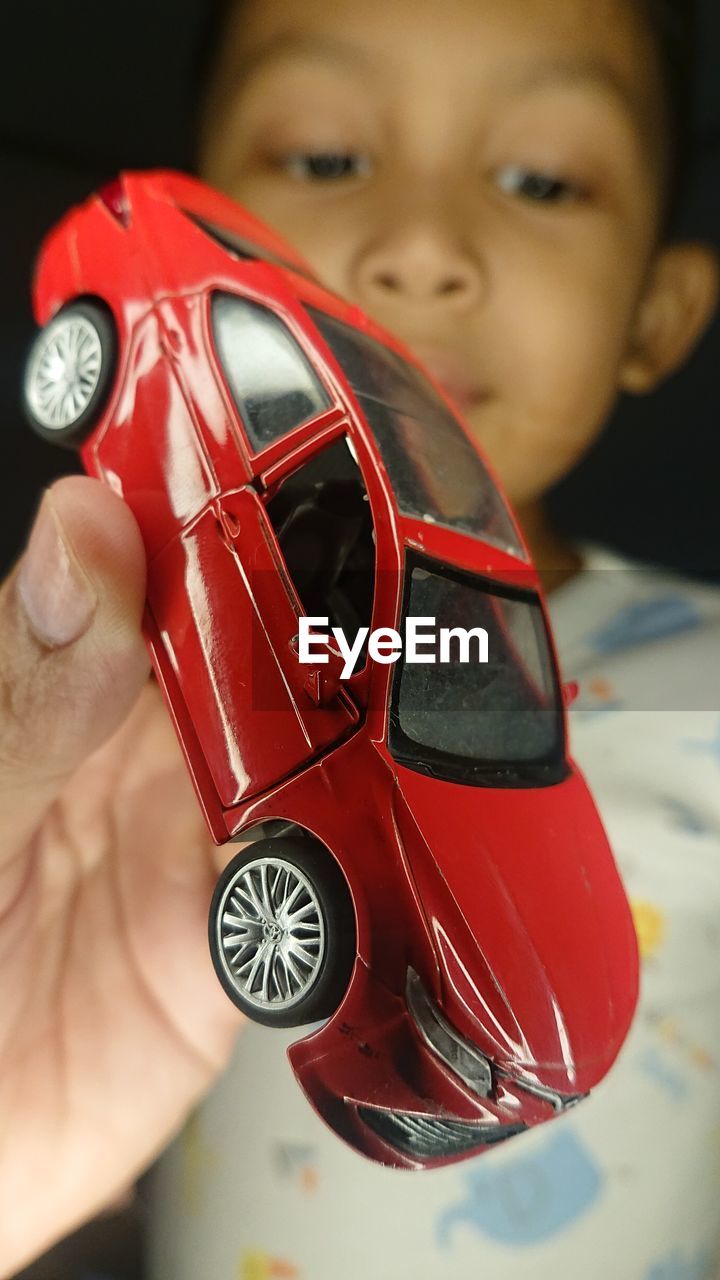 car, red, vehicle, childhood, motor vehicle, automobile, model car, child, mode of transportation, one person, land vehicle, toy, transportation, close-up, indoors, focus on foreground, toy car, men, hand, holding, headshot, portrait