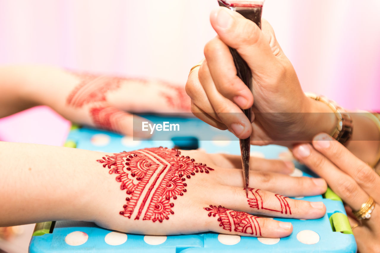 Cropped image of beautician masking henna tattoo on bride hand during wedding
