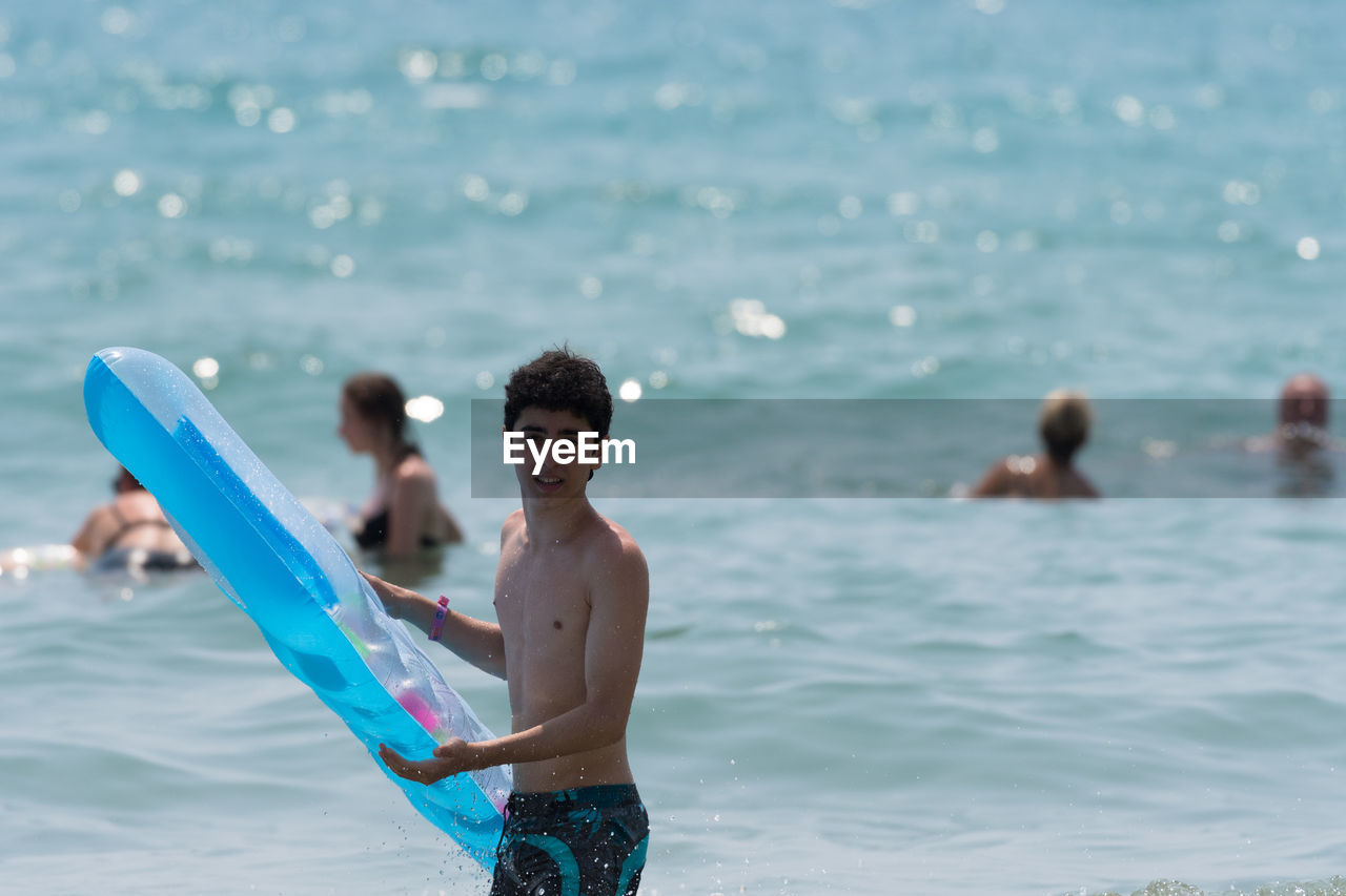 Portrait of teenage boy holding inflatable raft at beach