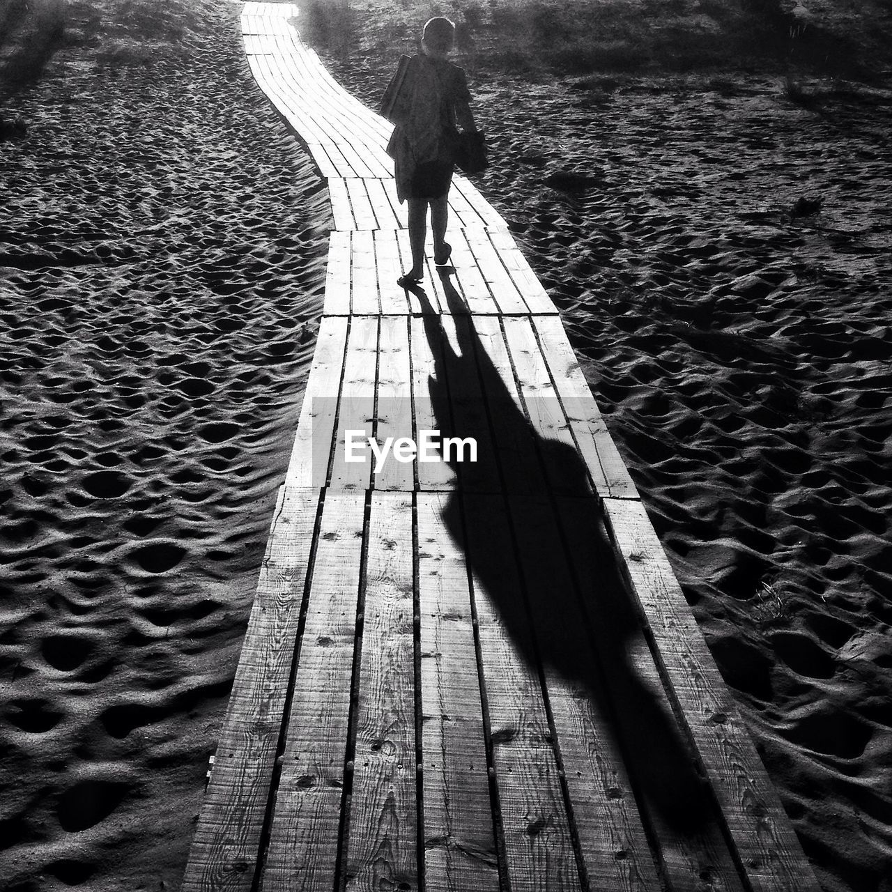 Beach scene. young boy casting shadow on wood walkway 