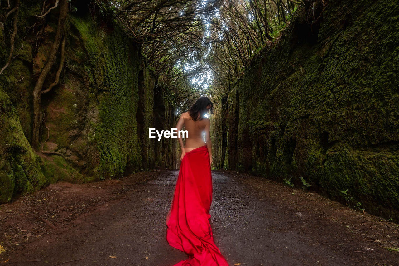 Shirtless woman wrapped in red fabric at forest