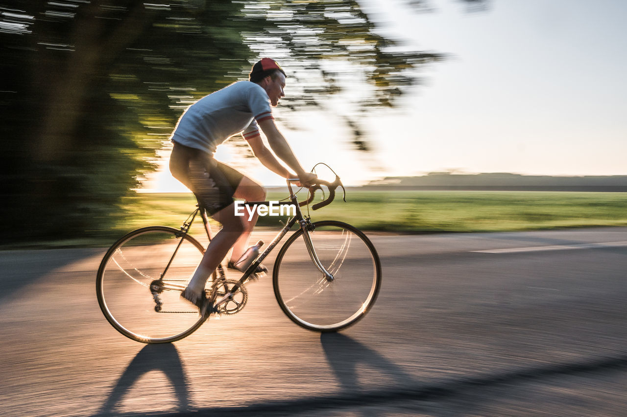Blurred motion of man riding bicycle on road during sunny day