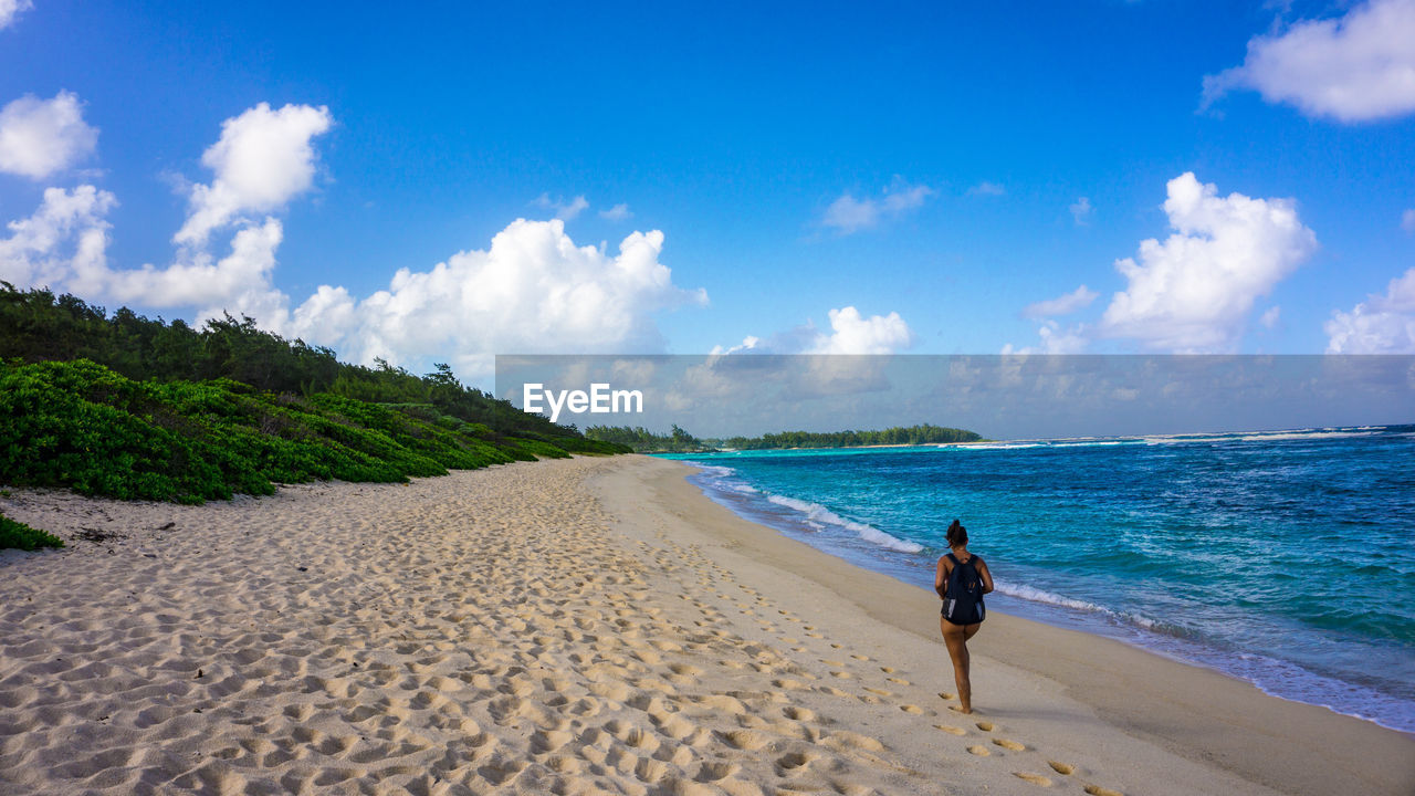 Woman walking on beach against blue sky