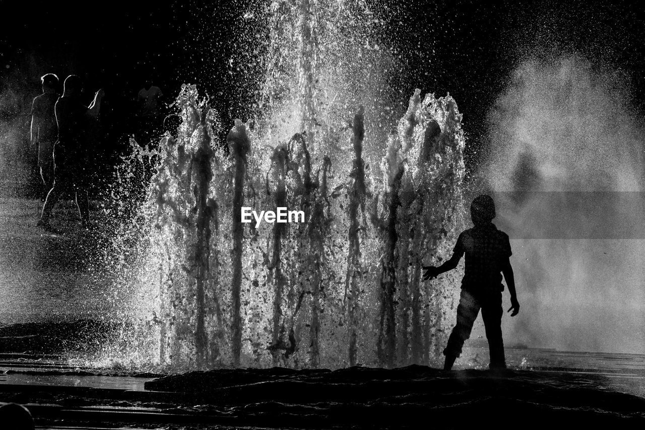 Silhouette boy standing by fountain at night