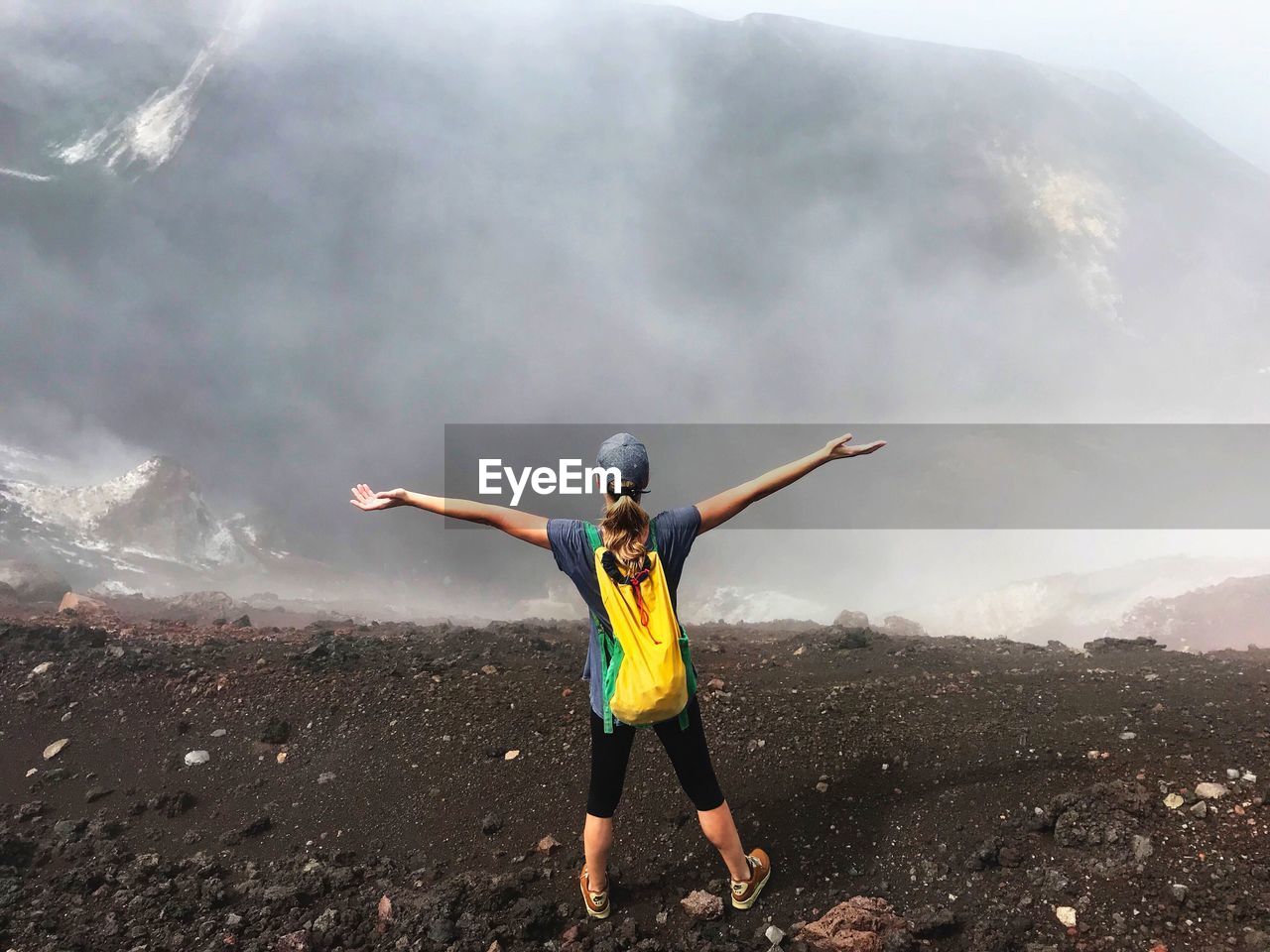 Rear view of young woman with arms outstretched standing on mountain during foggy weather