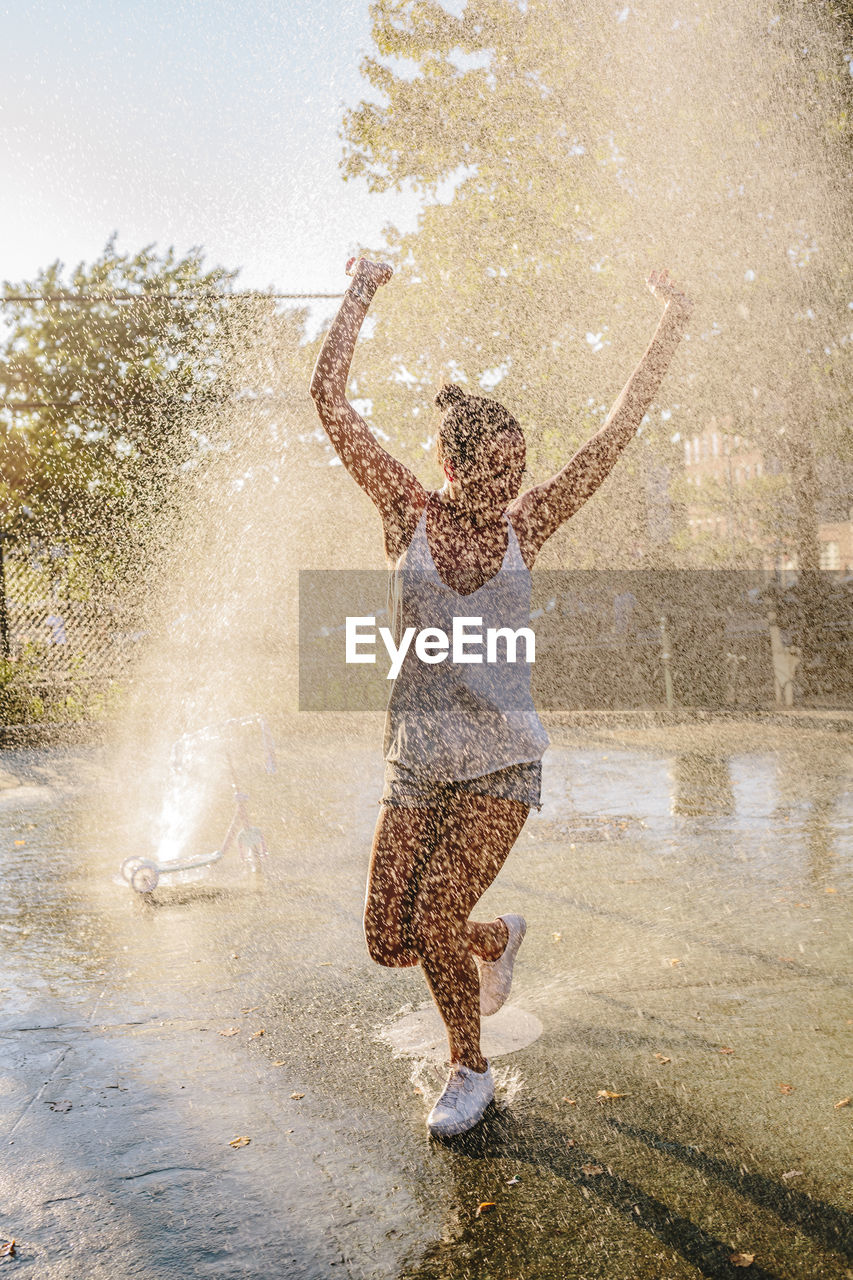 Young woman jumping water jet of a fountain