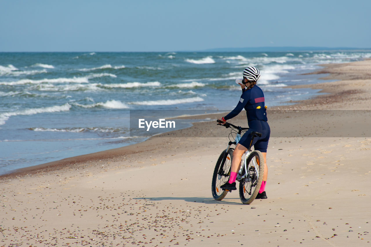 SIDE VIEW OF BOY RIDING BICYCLE ON BEACH