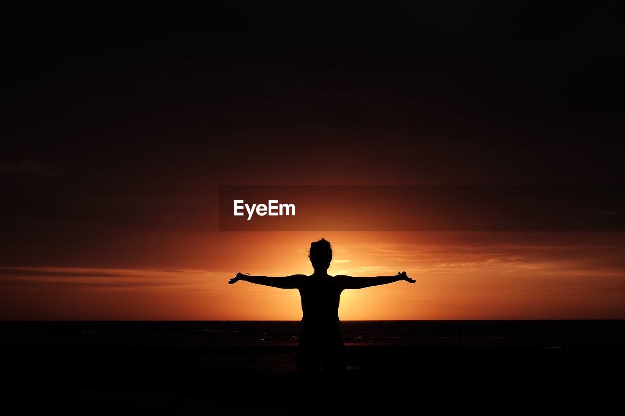 Silhouette of person standing on beach at sunset