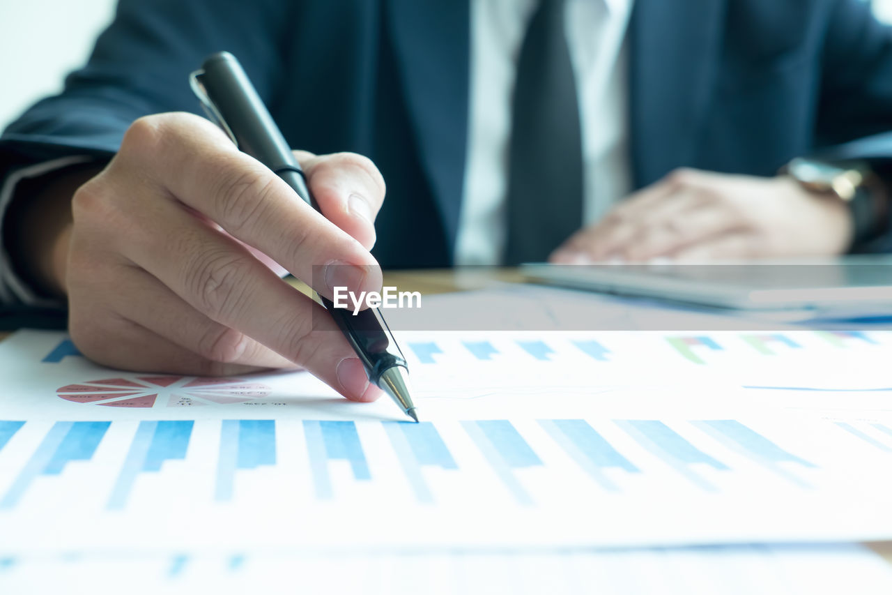 Midsection of man analyzing graphs on desk