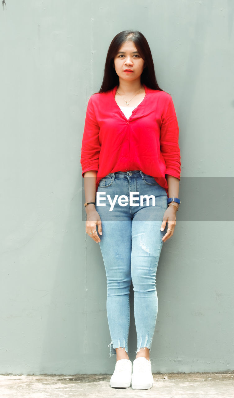 Portrait of young woman standing against wall