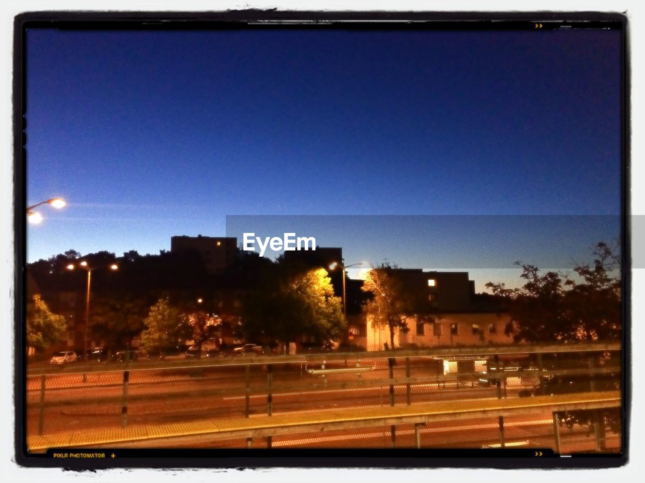 Illuminated street by buildings against clear sky during sunrise