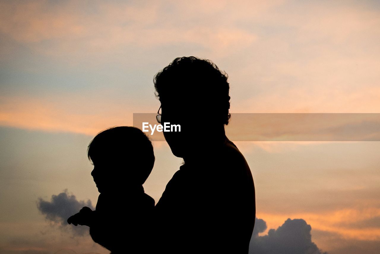 Silhouette father and son against sky during sunset