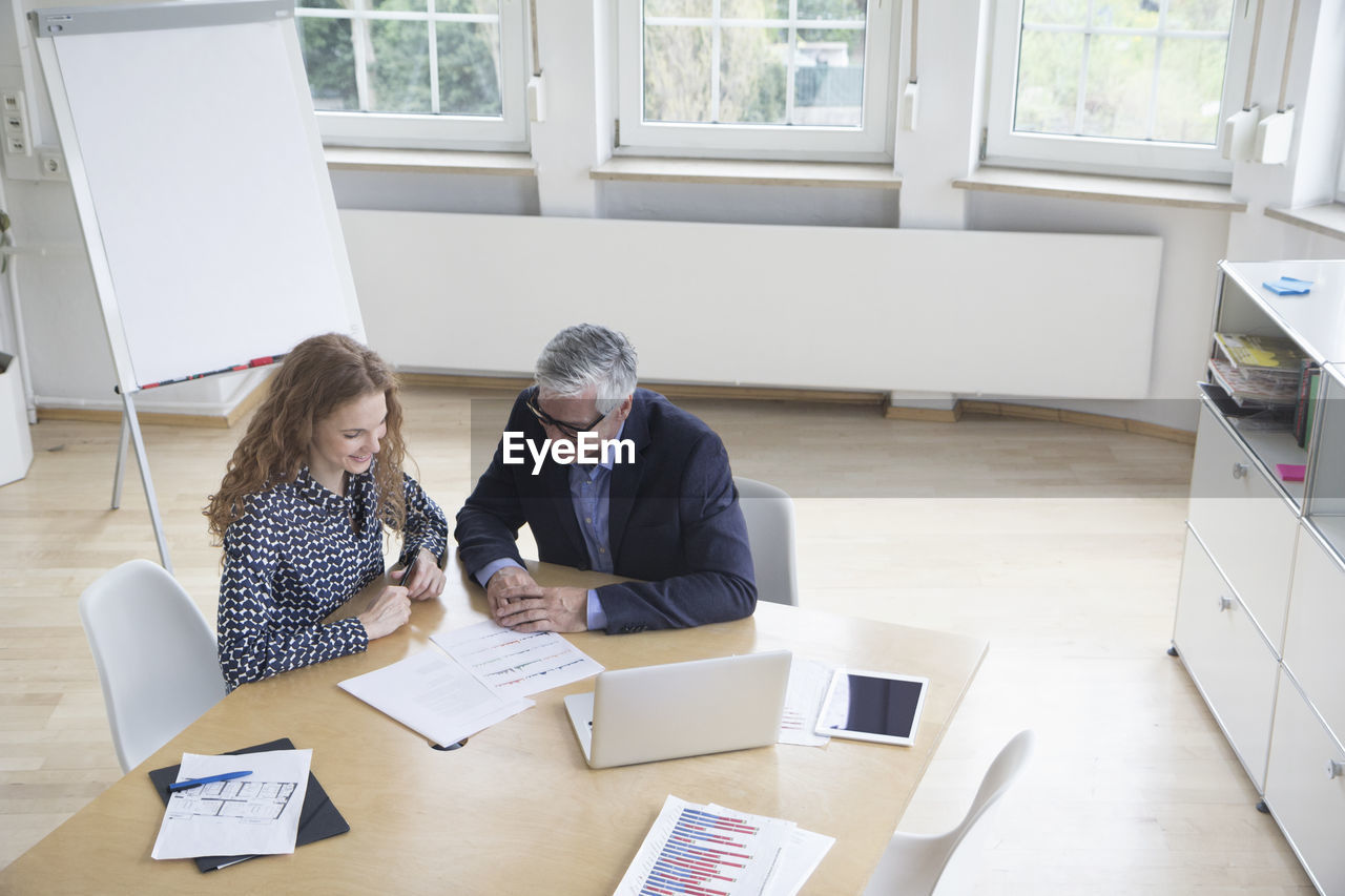 Businessman and woman sitting at boardroom table looking at documents