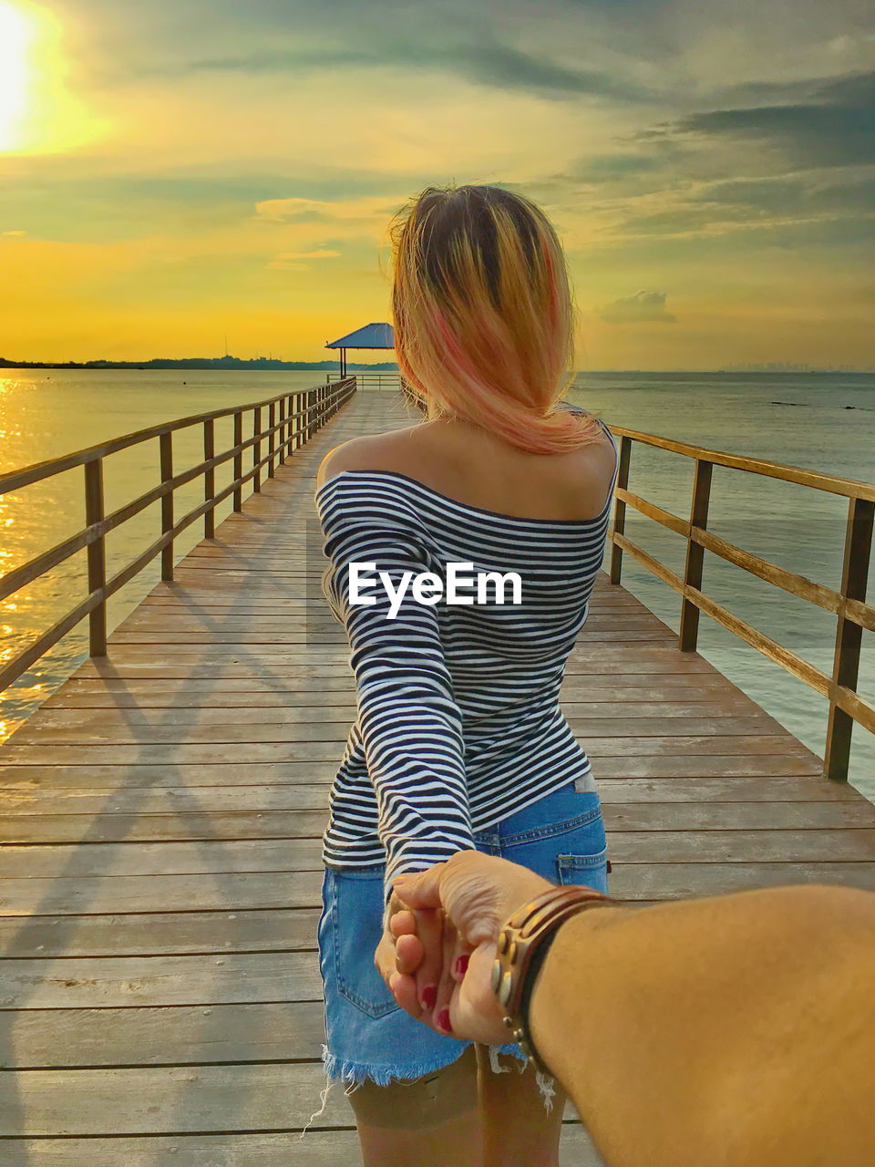 Woman holding cropped hand while standing on pier over sea