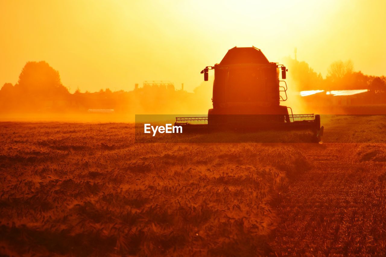 Combine harvester on field against sky during sunset