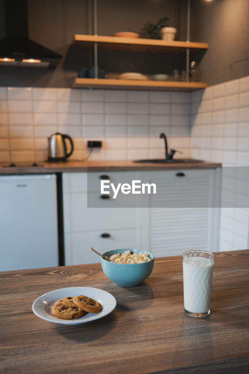 Plate with tasty oatmeal biscuits with chocolate chips against glass of milk on wooden table