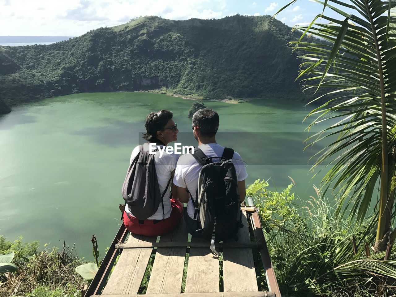 Rear view of couple sitting on observation point by lake