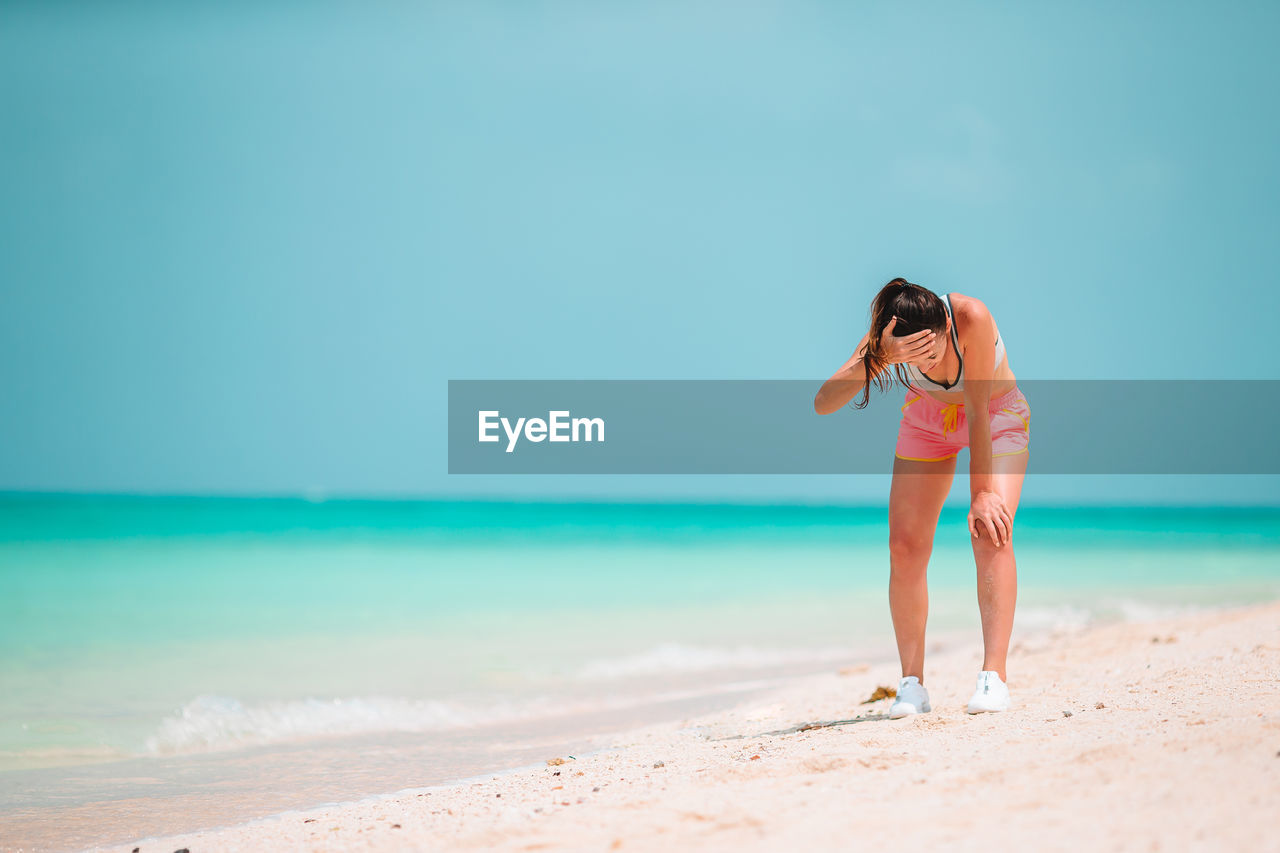 WOMAN STANDING ON BEACH AGAINST SEA