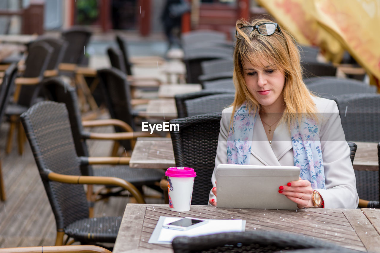 Woman using digital tablet while sitting at sidewalk cafe in city
