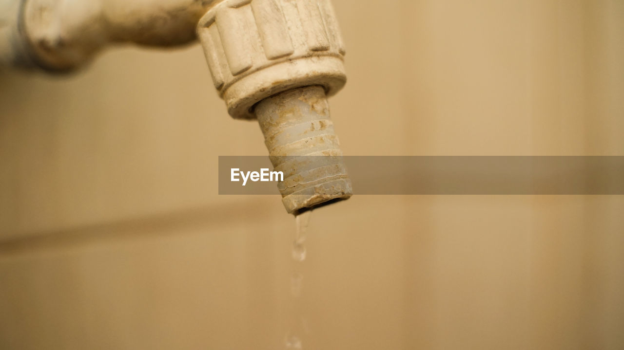 Close-up of water drop falling from faucet against wall