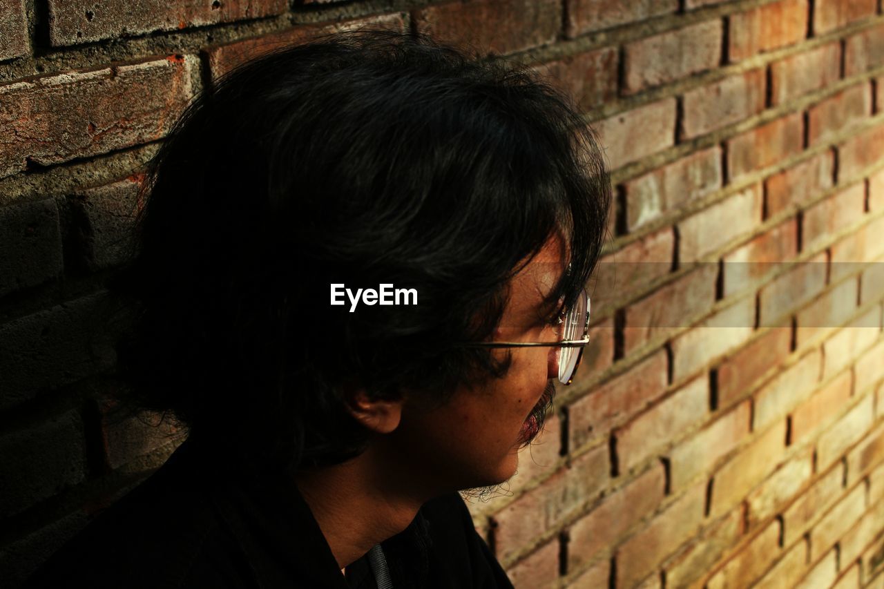 Close-up of young man leaning on brick wall